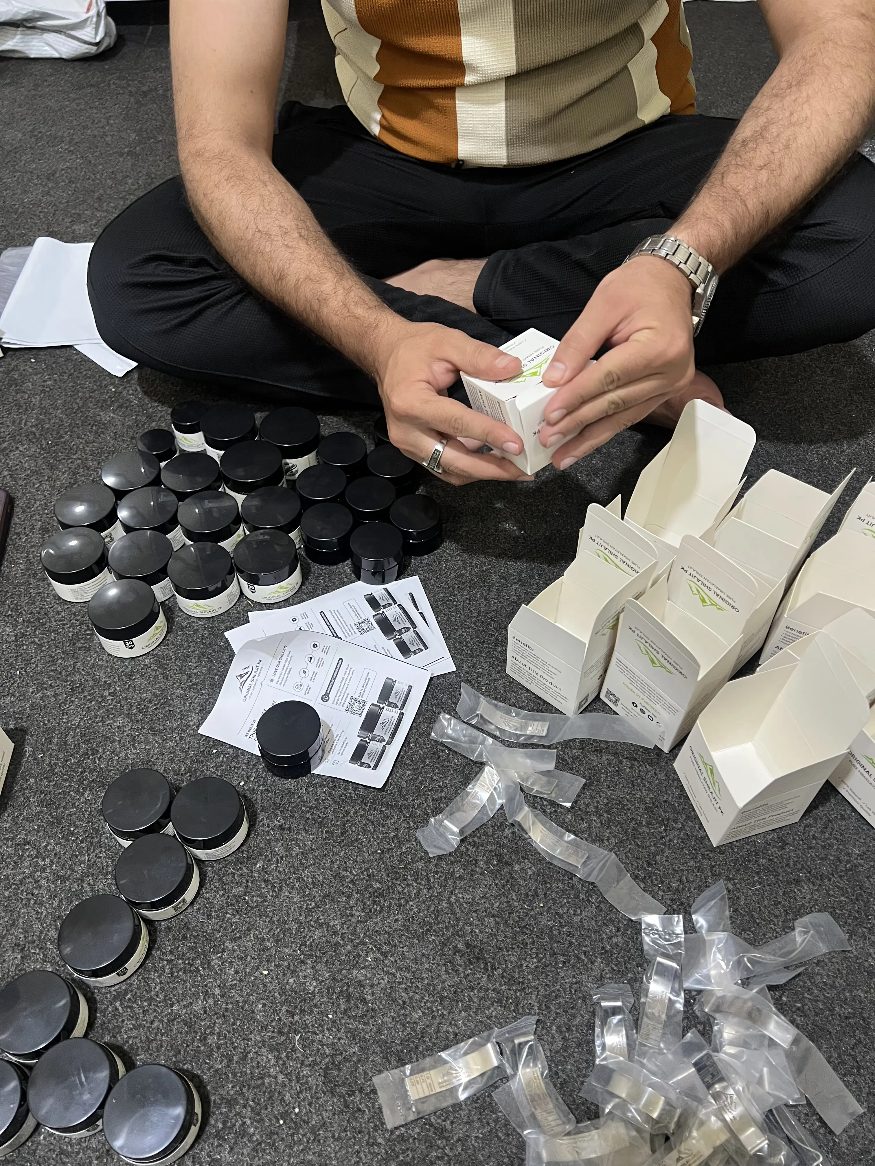 Original Shilajit PK boxes being folded by hand next to jars and usage guides